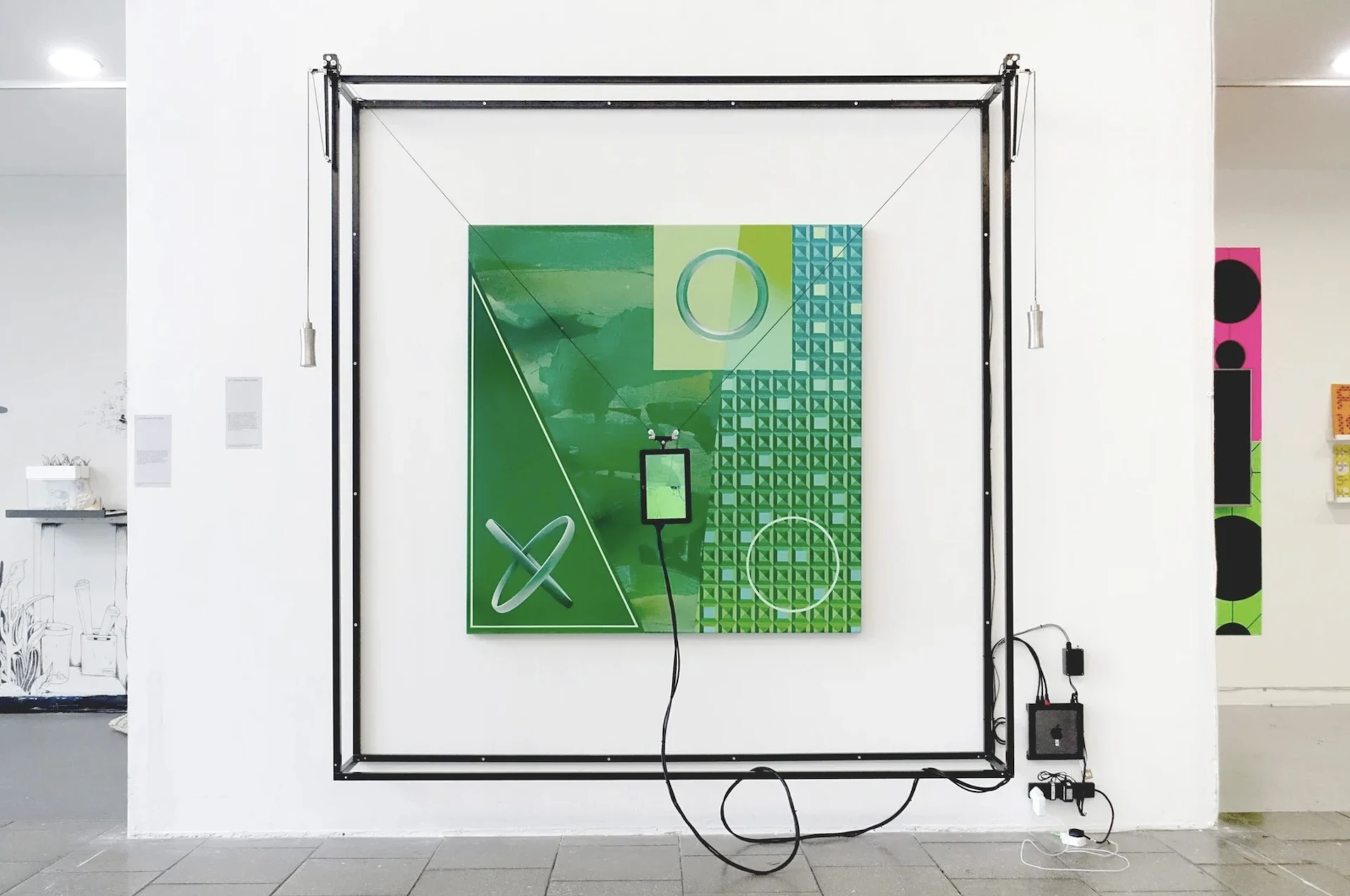 Installation view of the piece, a green painting mounted on the wall with a frame surrounding it and a computer screen on a pulley syste moving across it.