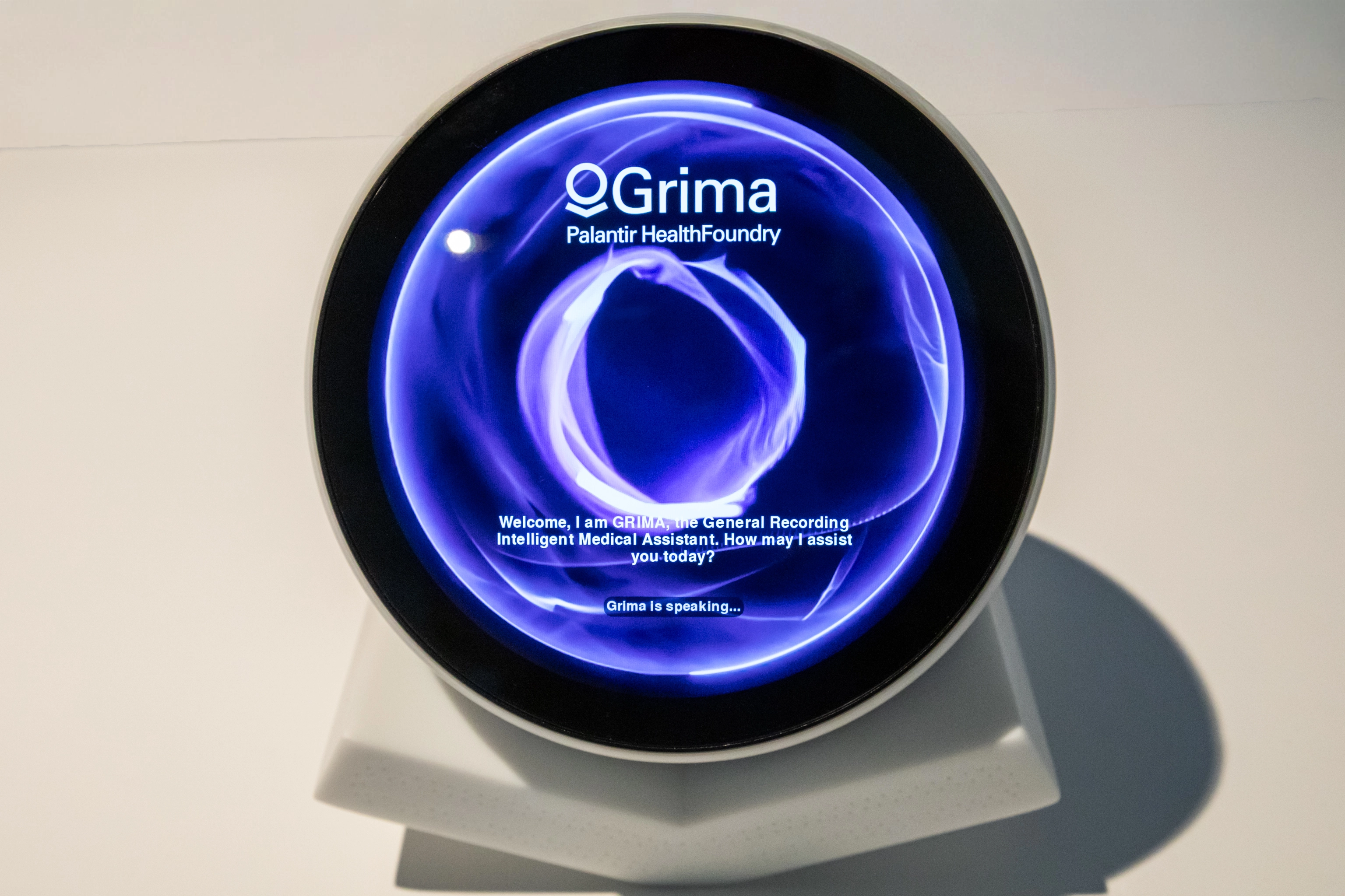 An image showing the device on a white plinth.  The device resembles the Palantir logo and has a circular screen embedded in it.