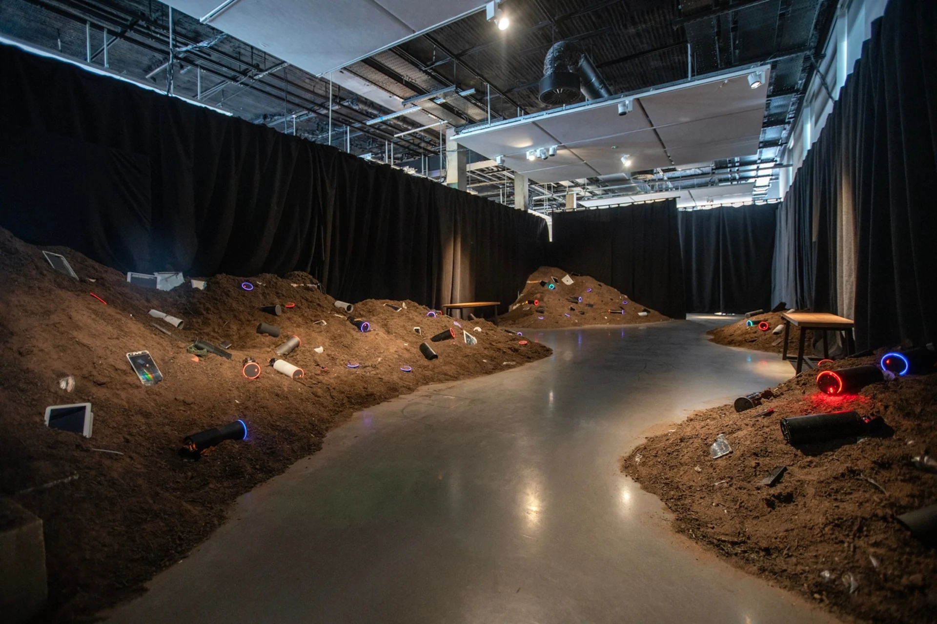 Installation view of the work, showing 6 tonnes of soil in a room, with 200 buried smartphones and smart speakers